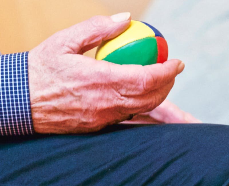 Elderly man holding a colorful therapy ball indoors, promoting relaxation and health.